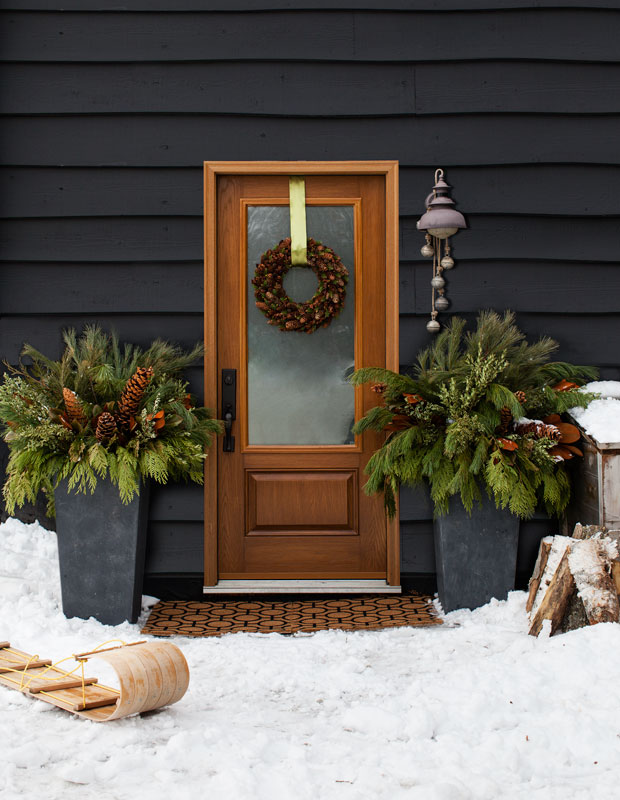 Holiday curb appeal — a wooden doorway with bunches of evergreen and a pinecone wreath