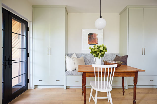 Breakfast nook with a vintage-inspired wood table, white seating and a banquette in between cabinetry