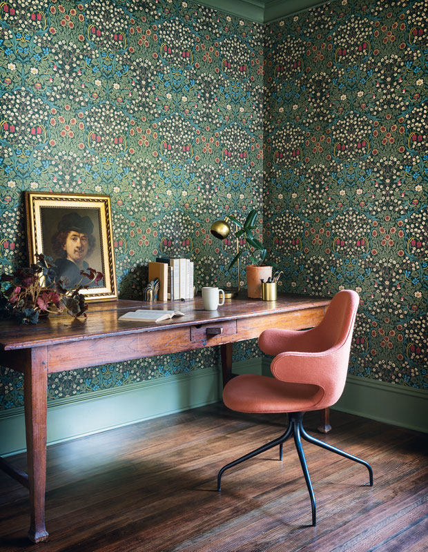 A study room with floral green wallpaper and a wooden desk.