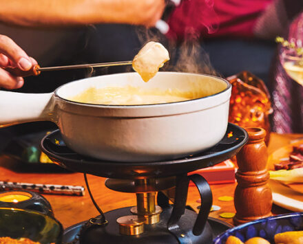 Person's hand dipping fried bread in cheese fondue