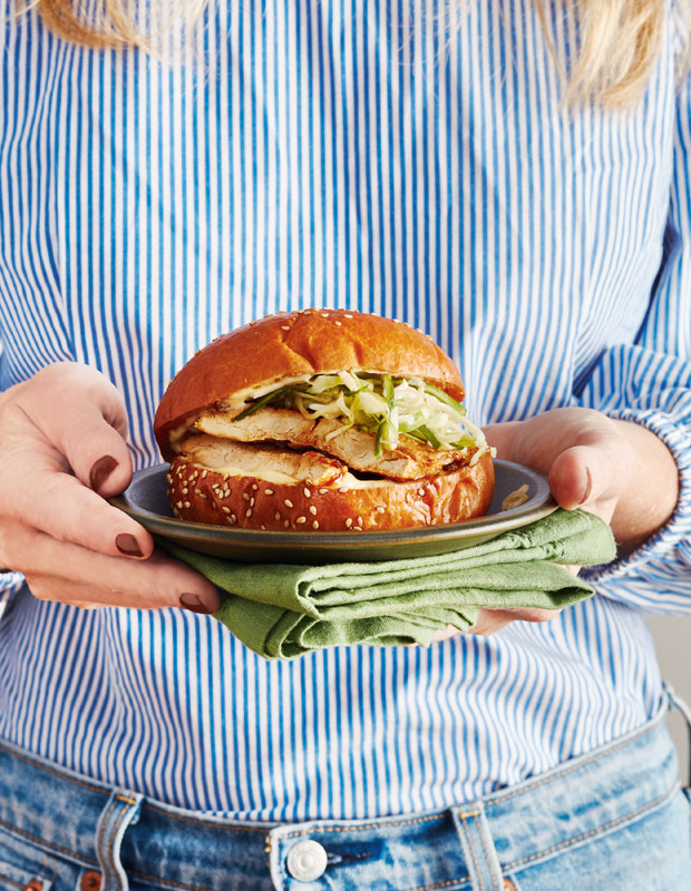A woman holds a Soy & Hot Honey-Glazed Faux Chicken Sandwich on a plate.