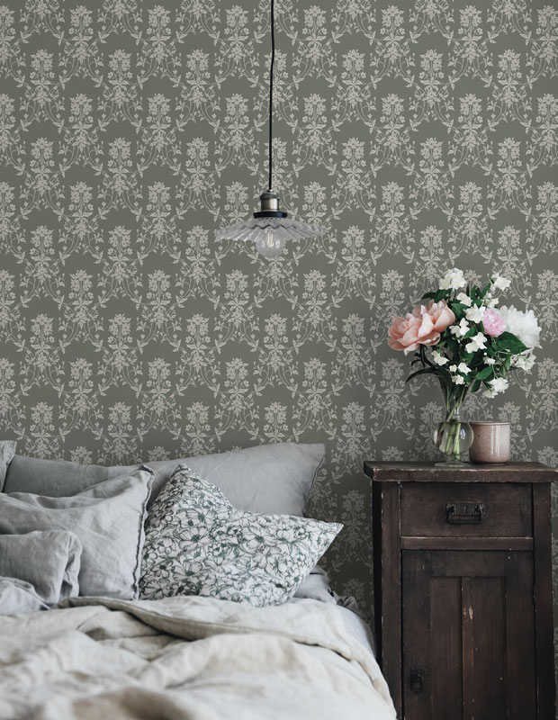 A bedroom with pale greenfloral wallpaper and a floral pillow.