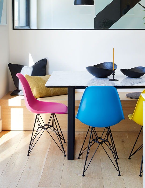 Two bright chairs in pink and blue at a dining table in the February kitchen of the month.