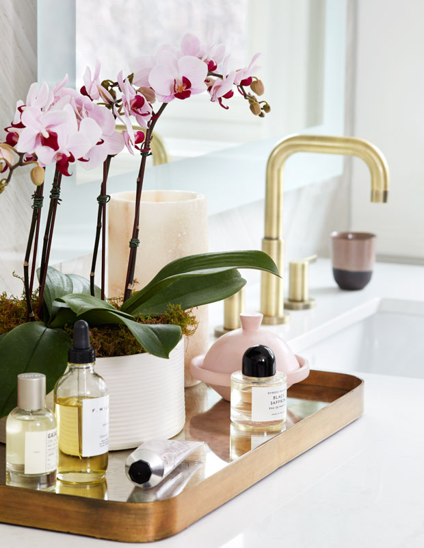 Bathroom counter with a gold faucet and a toiletry tray with live orchids.