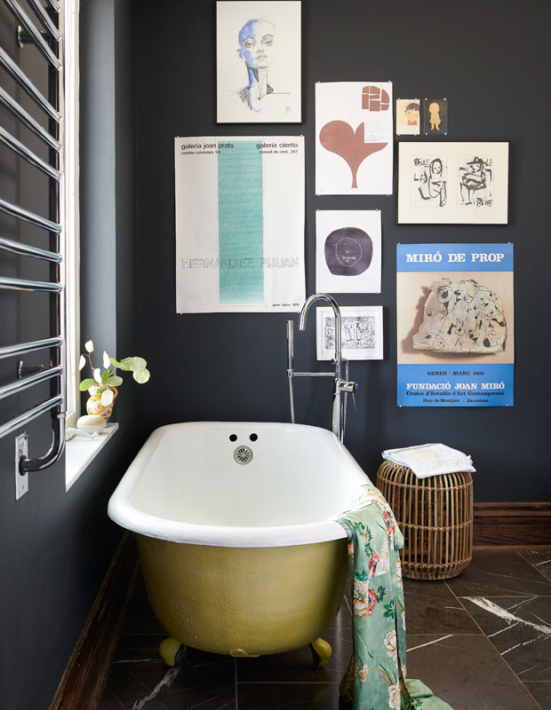 A black bathroom with art prints on the wall and a gold tub