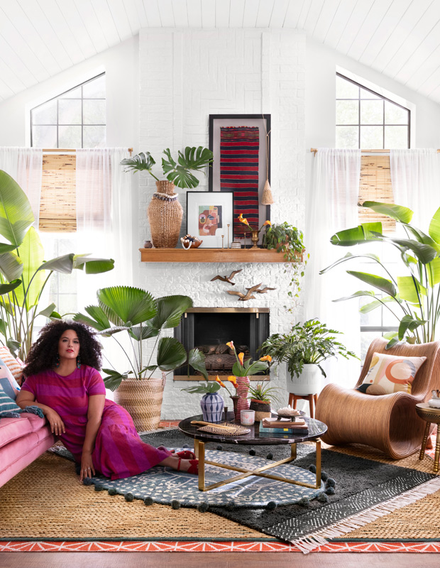 Justina Blakeney lies in a living room filled with plants and rattan accents
