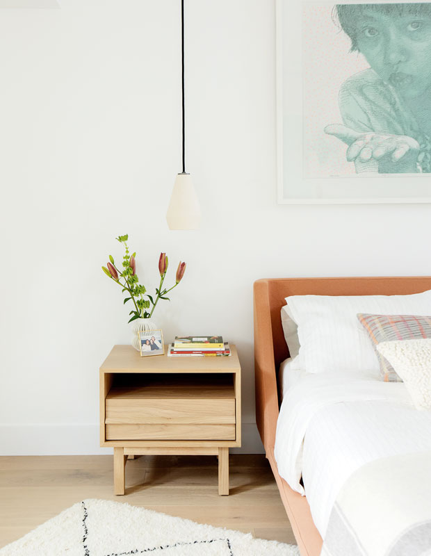 After shot of a principal bedroom with a wooden bedside table and white pendant light