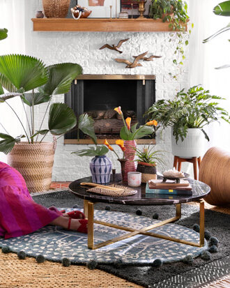 Justina Blakeney lies in a living room filled with plants and rattan accents