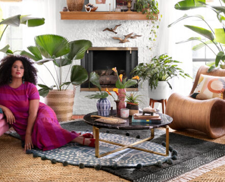 Justina Blakeney lies in a living room filled with plants and rattan accents
