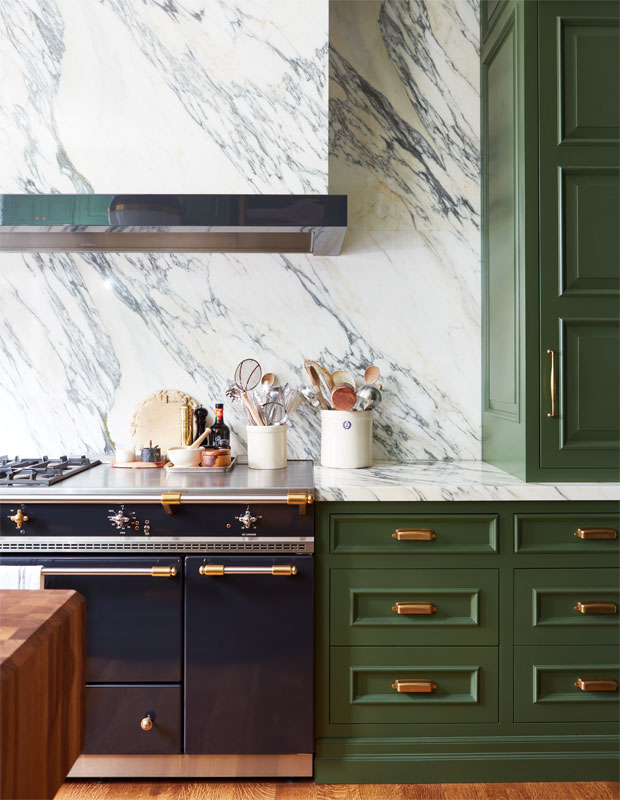 Green kitchen with marble countertop and backsplash.