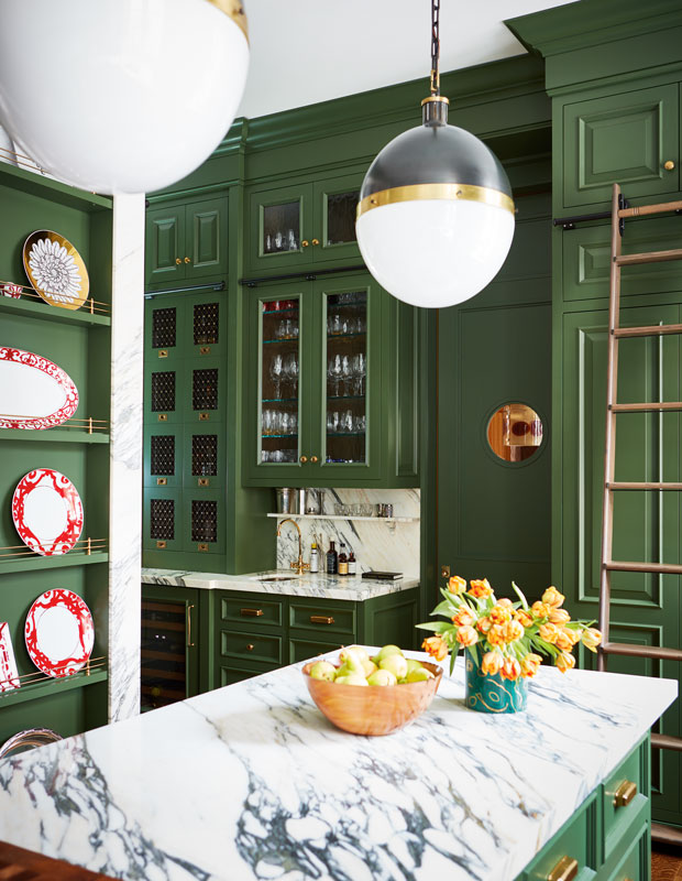 Green kitchen with marble countertop and round pendant lights.