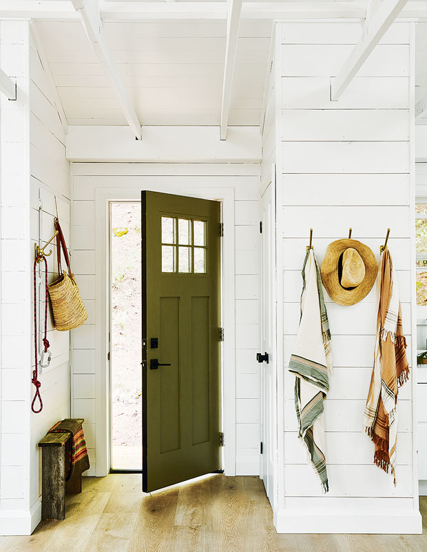 Entryway with white paneled walls and a green door. Hats and scarves are hung on wall hooks