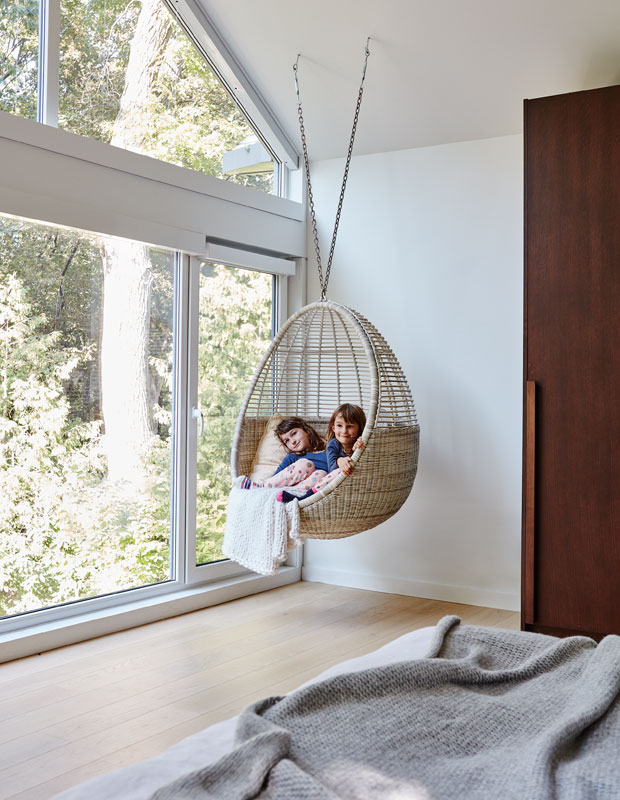 Modern Century Home principal bedroom with a hanging wicker chair swing. The homeowners' two young daughters sit in the swing by the window.