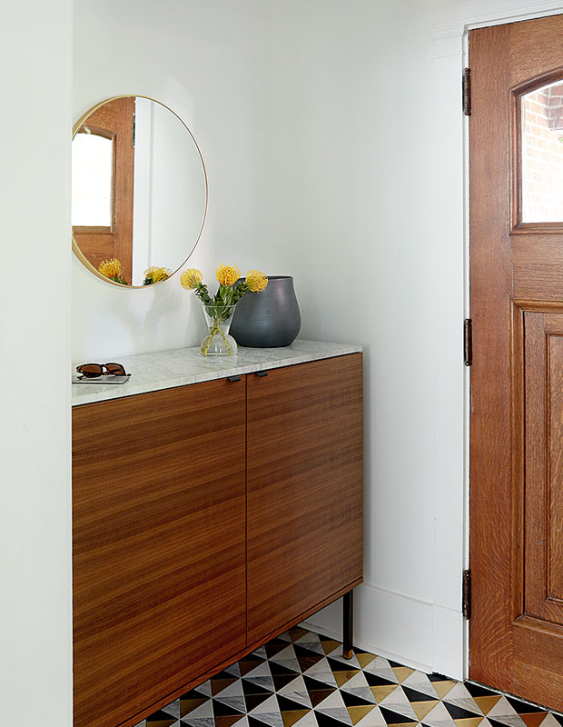 Entryway with a dark wood door and matching set of drawers with a mirror over it.