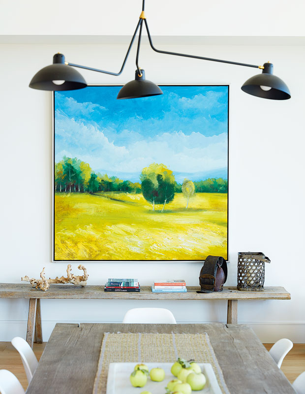 Dining area with a bright painting of a yellow field under a blue sky. A black light fixture hangs from the ceiling.