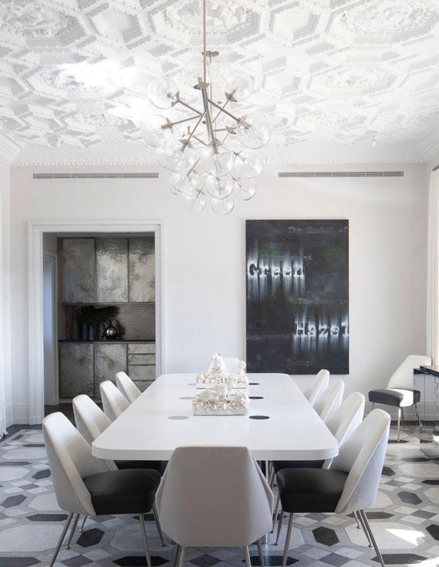 White dining room with an intricately carved ceiling of hexagons and floral patterns