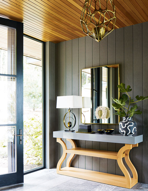 Entryway with vertical green panelled walls and a small side table with a mirror over it.