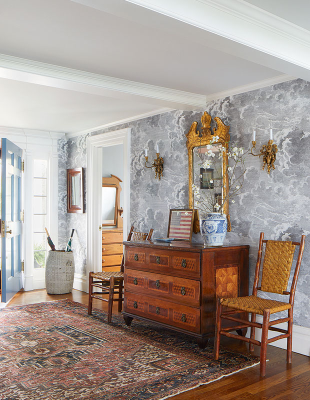 Entryway with a vintage chest of drawers, two chairs and periwinkle wallpaper.