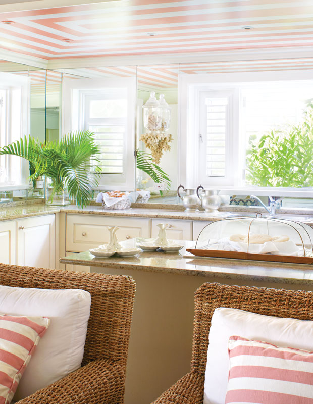 Kitchen with coral pink striped ceiling and matching chair pillows, with large green plants in the room.