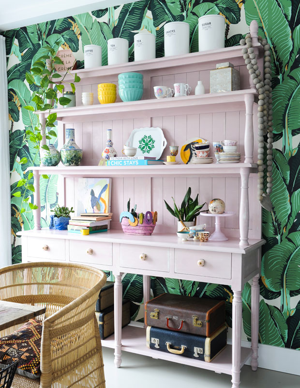 Kitchen with plant-themed wallpaper and a baby pink shelf displaying dishes and pastel knick-knacks.