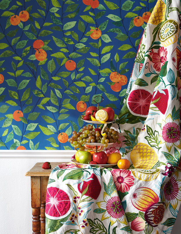 Dining area with dark fruity wallpaper, a curtain covered in fruit designs and a table with a bowl of fruit.