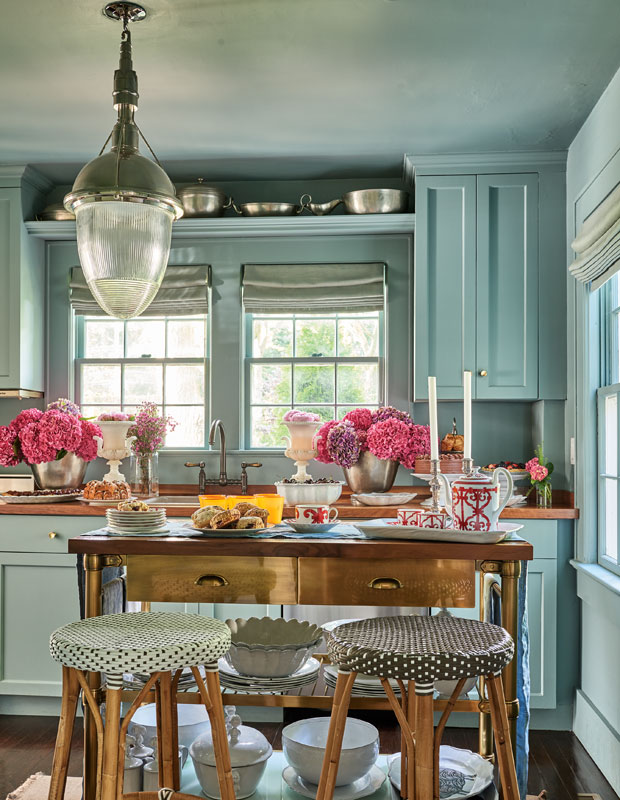 Seafoam green kitchen with hot pink flowers in vases and a vintage glass light hanging from the ceiling.
