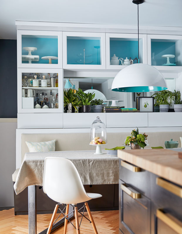 White kitchen with painted bright blue accents on inside of light shade and backboards of see-through cabinetry.