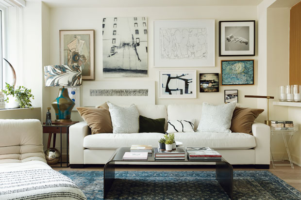 Beige living room with art hung all over the wall and tons of pillows on a white couch.