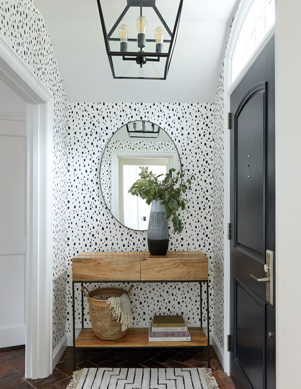 Entryway with black and white wallpaper, oval wall mirror and a small shelf for storing objects.