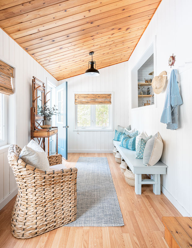 Entrance hallway with pale wood ceiling and floor, a small bench and a wicker chair.