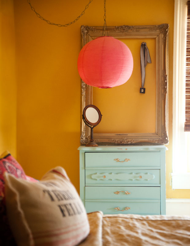 A bedroom with sunset colors, like a bright pink pendant light fixture and yellow-orange walls.