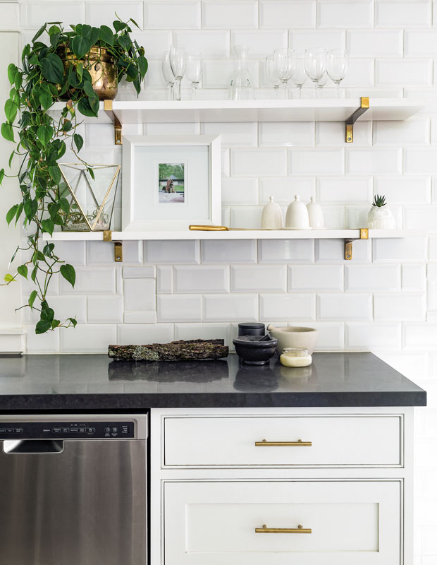 Kitchen wiht white tiled walls and floating shelves with potted plants.