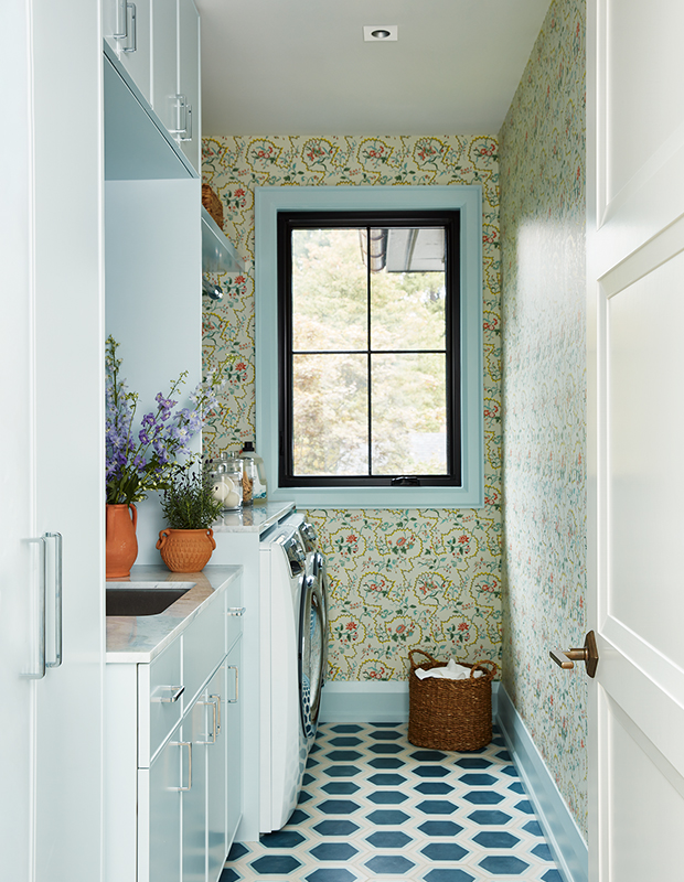 A colorful laundry room designed by Jennifer Overweel features geometric floor tile, patterned wallpaper and built-in storage.