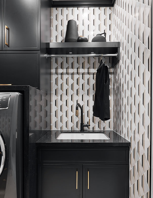 This black and white laundry room has a high-contrast look with black cabinets and graphic mosaic wall tile that complements the hits of gold on the cabinet hardware and plumbing fixtures.