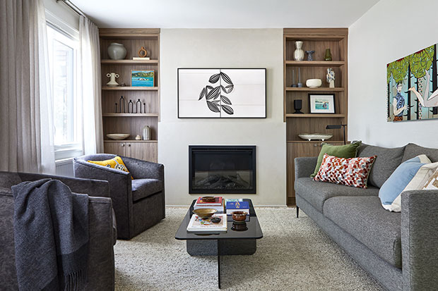 A clean and clearly new living room with grey couch, black chairs, and double cabinets which surround a TV and fireplace. little italy home renovation