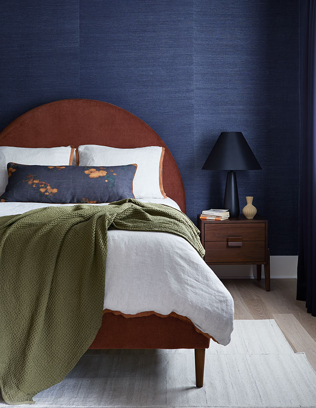 A mature bedroom with an MCM style bed with a rounded backboard, navy blue textured walls, and earth toned decor little italy home renovation