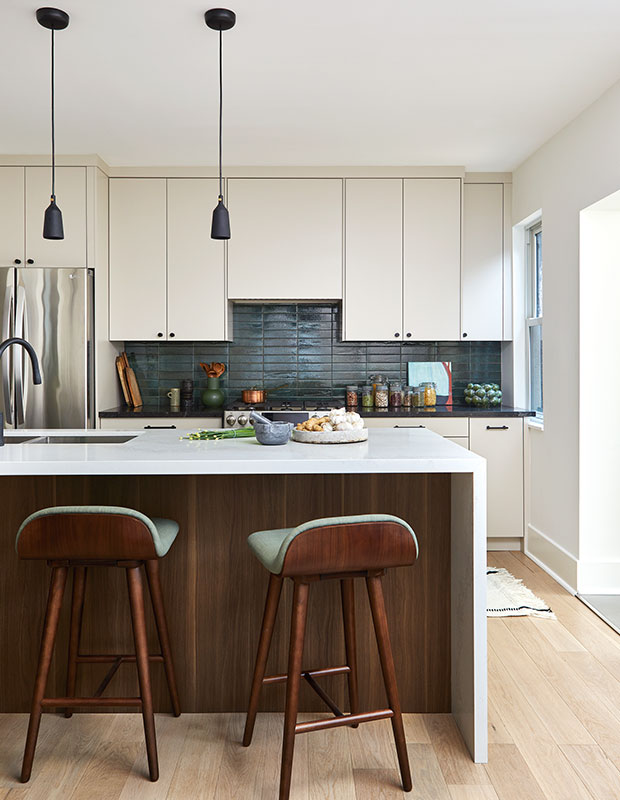 A classic modern kitchen with deep-green rectangular tile backsplash, black countertops, and a large island with dark wood detailing. little italy home renovation