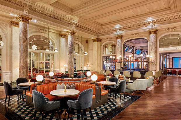 wide shot of a luxurious restaurant dining room with deep orange leather booths and plush suede chairs. The walls and columns are are white marble bathed in soft white light emitted from modern orb lighting fixtures. The floor is an intricate diamond patterned tile. calgary travel guide