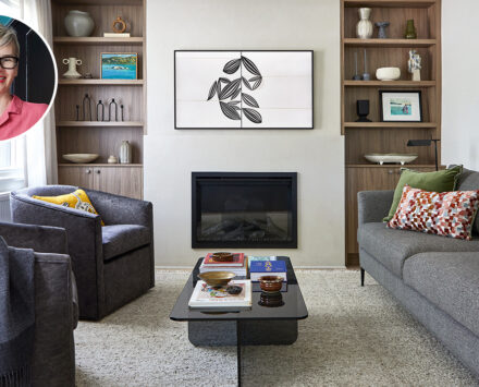 A clean and clearly new living room with grey couch, black chairs, and double cabinets which surround a TV and fireplace.