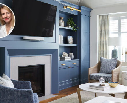 A clean, classic, modern living room with blue and grey decor, gold accents and hardware, and a white panelled ceiling. In the corner of the image sits a bubble portrait of the two designers, who are both blonde women.