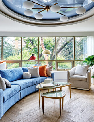 A wide shot of a living room with blue accents, large windows, and eclectic art pieces and sculptures