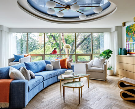 A wide shot of a living room with blue accents, large windows, and eclectic art pieces and sculptures
