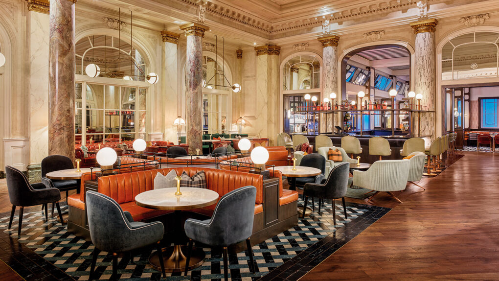 wide shot of a luxurious restaurant dining room with deep orange leather booths and plush suede chairs. The walls and columns are are white marble bathed in soft white light emitted from modern orb lighting fixtures. The floor is an intricate diamond patterned tile.