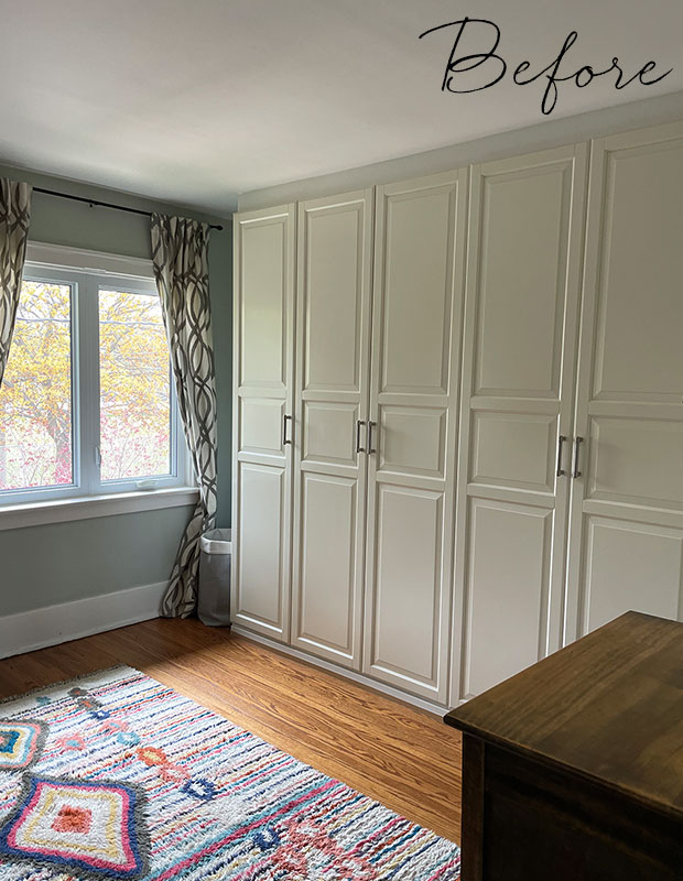 Before: a beige floor to ceiling closet unit with five narrow doors takes up one wall of this bedroom, which has medium hardwood floors, a colourful rug, and a patterned black and white curtain at the window. little italy home renovation