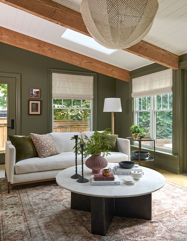 A living room with deep-green walls, natural wood beams on high ceilings, and furnished with modern rounded furniture, in cool shades of white. modern heritage townhouse