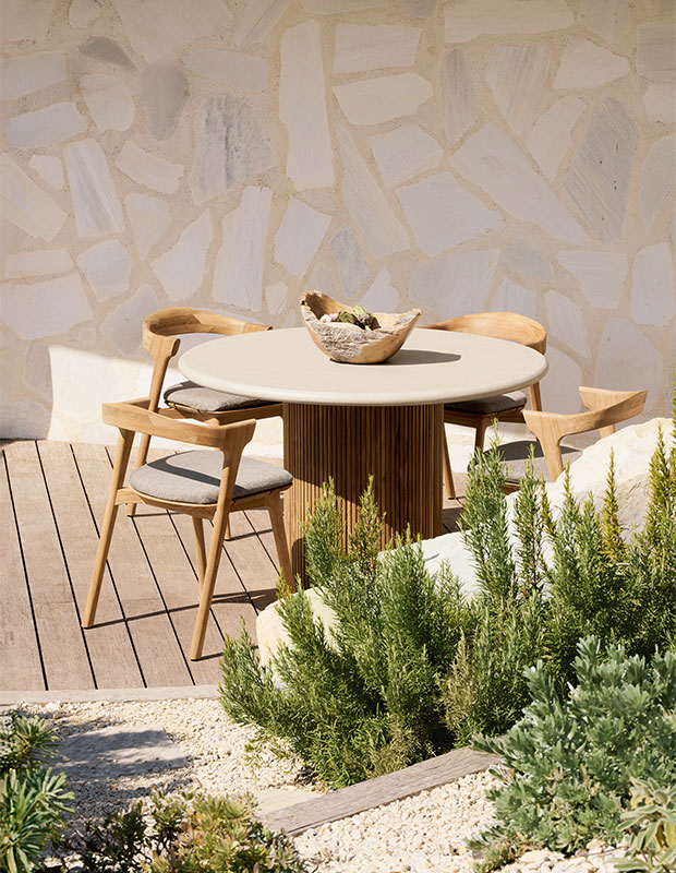 an outdoor dining table with a cylindrical base in the middle and a flat circular table top jutting out from above sits with chairs on a patio. sustainable summer accents.