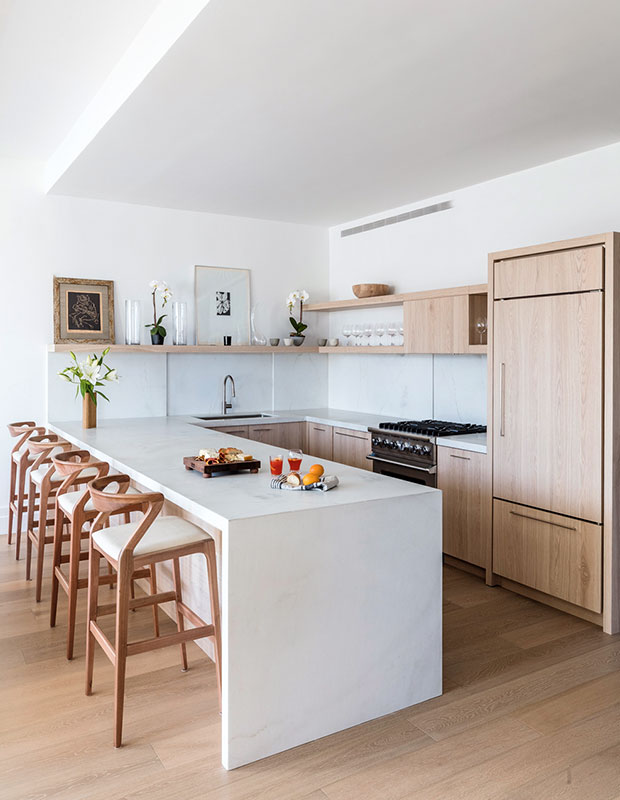 A white kitchen with a large marble island, blonde wood cabinets and chairs, and matching wood floors. kitchen design advice