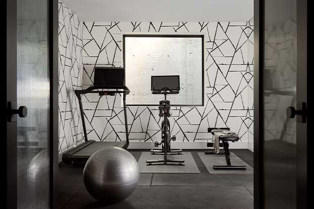 A very modern home-gym with black and white geometric wallpaper. A treadmill, a stationary bike, a weight-lifting station, and a yoga ball are featured. english cottage-style house