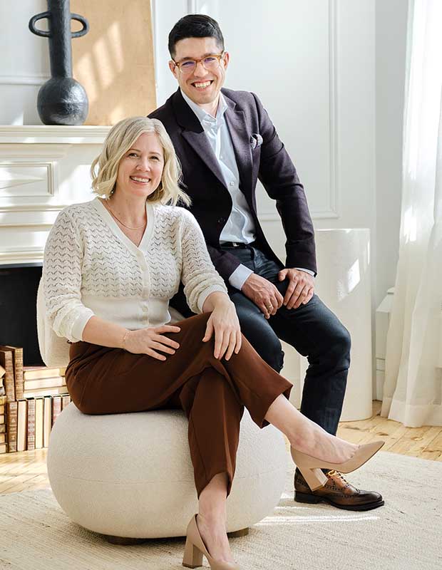Two caucasian individuals sit in a brightly lit room. One is a blonde woman, the other a dark haired man. english cottage-style house
