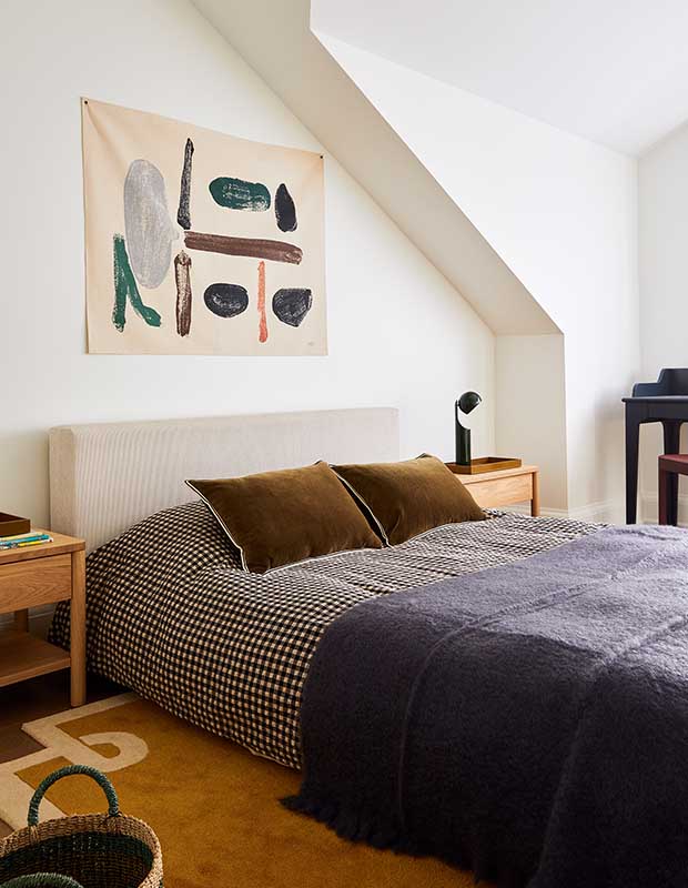 The second bedroom has a checked comforter, a plush fuzzy blanket, warm-toned rug, and abstract art hangs on the wall. serene city retreat